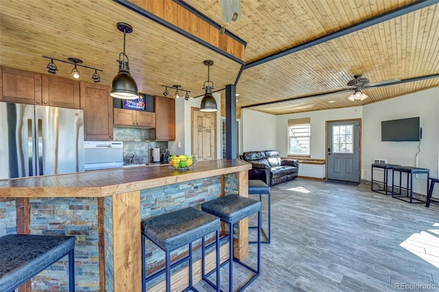 kitchen featuring wooden ceiling, ceiling fan, a breakfast bar area, freestanding refrigerator, and backsplash