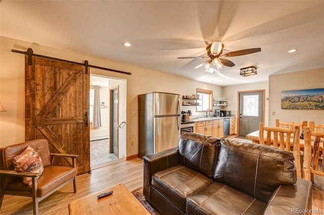 living room with recessed lighting, light wood-style flooring, a barn door, ceiling fan, and baseboards