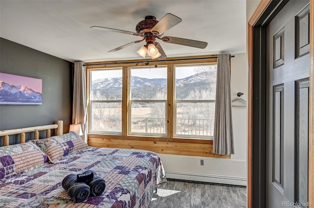 bedroom with a ceiling fan, a mountain view, baseboard heating, and wood finished floors