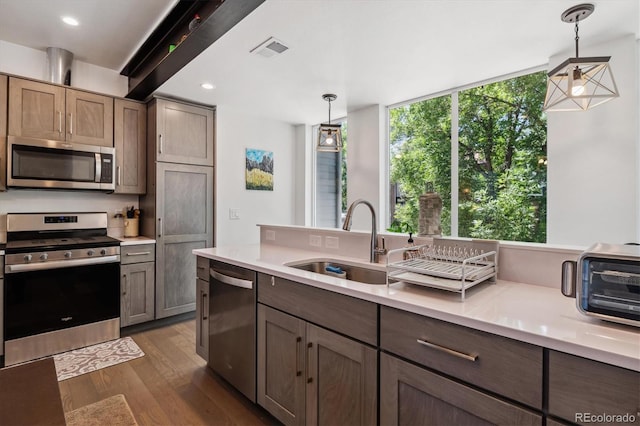 kitchen with dark wood-type flooring, stainless steel appliances, sink, and pendant lighting