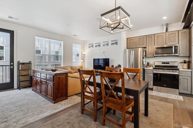 kitchen featuring light wood-type flooring, stainless steel appliances, an inviting chandelier, and decorative light fixtures