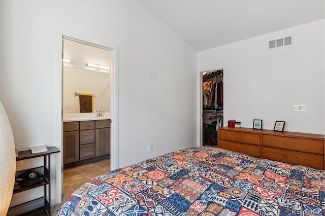 bedroom with ensuite bath, vaulted ceiling, light tile patterned flooring, a closet, and a walk in closet