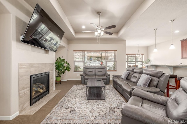 living area with carpet floors, baseboards, ceiling fan, a fireplace, and a raised ceiling