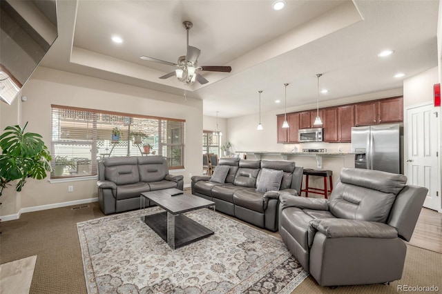 living room featuring a tray ceiling, a ceiling fan, baseboards, recessed lighting, and light colored carpet