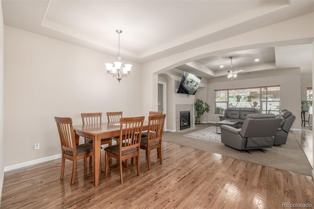 dining space featuring a raised ceiling, baseboards, wood finished floors, a fireplace, and recessed lighting