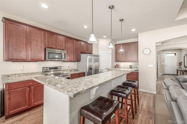 kitchen with appliances with stainless steel finishes, arched walkways, light wood finished floors, a breakfast bar area, and recessed lighting