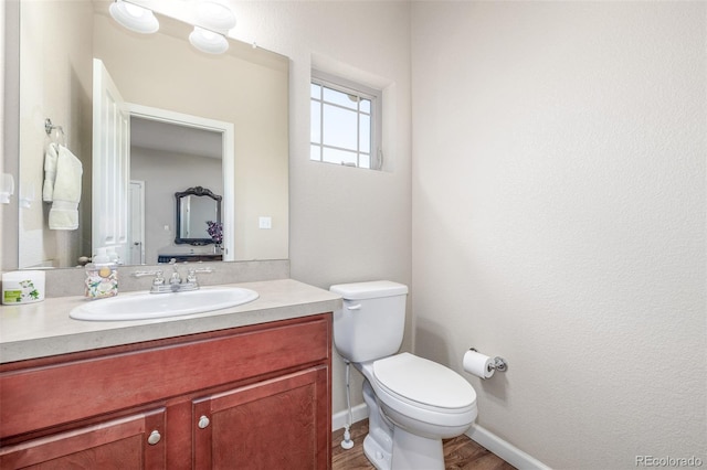 half bath featuring toilet, vanity, wood finished floors, and baseboards