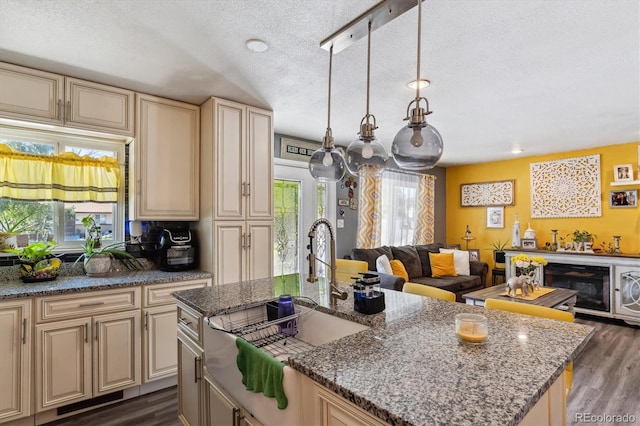 kitchen with light stone counters, a textured ceiling, decorative light fixtures, an island with sink, and sink