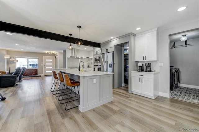 kitchen featuring pendant lighting, white cabinets, a kitchen island with sink, stainless steel appliances, and washer and clothes dryer