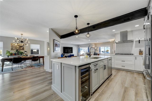 kitchen featuring light hardwood / wood-style flooring, a kitchen island with sink, wine cooler, decorative light fixtures, and wall chimney exhaust hood