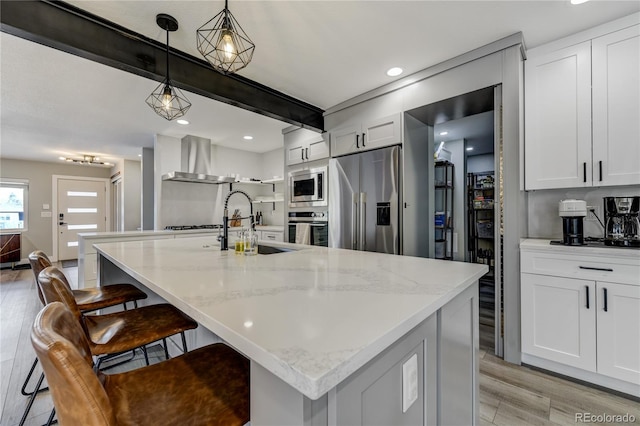 kitchen with wall chimney range hood, white cabinetry, appliances with stainless steel finishes, and pendant lighting