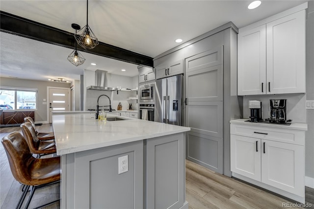 kitchen with hanging light fixtures, light stone counters, stainless steel appliances, beam ceiling, and wall chimney exhaust hood