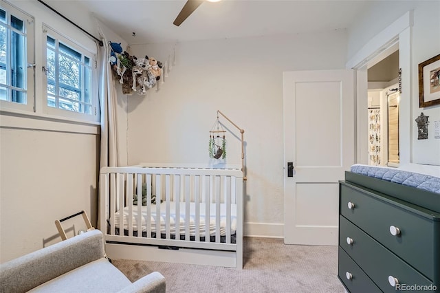 bedroom featuring a crib, ceiling fan, and light colored carpet