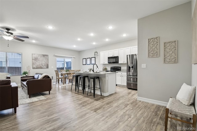 2328 Saddle Back Ct, Fort Lupton, CO 80621 - kitchen featuring black appliances, open floor plan, a breakfast bar, a kitchen island with sink, and white cabinetry