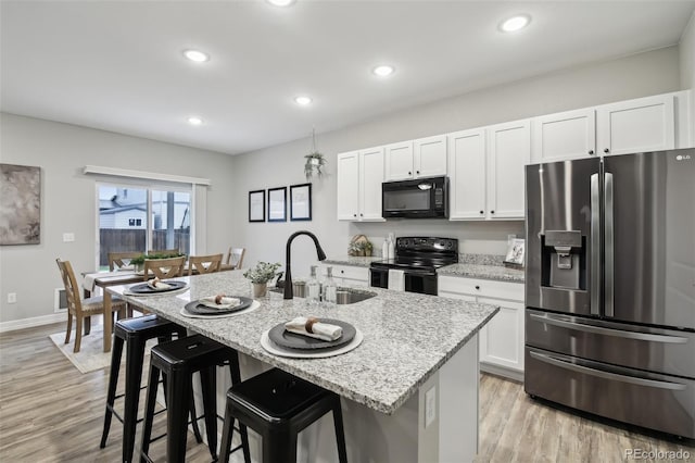 2328 Saddle Back Ct, Fort Lupton, CO 80621 - kitchen with black appliances, a sink, light wood-type flooring, a breakfast bar, and white cabinets