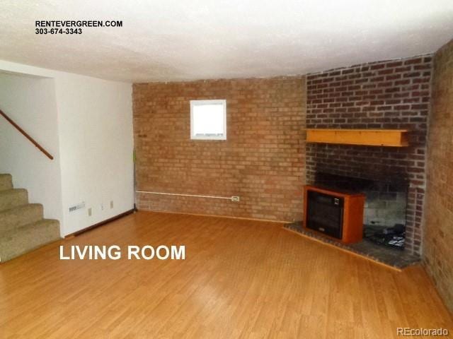 28127 Knowles Rd Unit A, B, & C, Evergreen, CO 80439 - unfurnished living room with wood finished floors, stairway, brick wall, and a brick fireplace