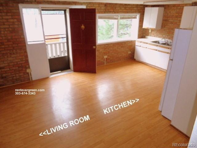 28127 Knowles Rd Unit A, B, & C, Evergreen, CO 80439 - kitchen featuring light wood-style flooring, brick wall, white cabinets, light countertops, and freestanding refrigerator
