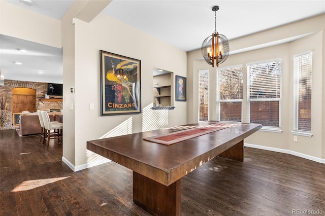 dining space featuring a chandelier, a brick fireplace, dark wood-type flooring, and brick wall