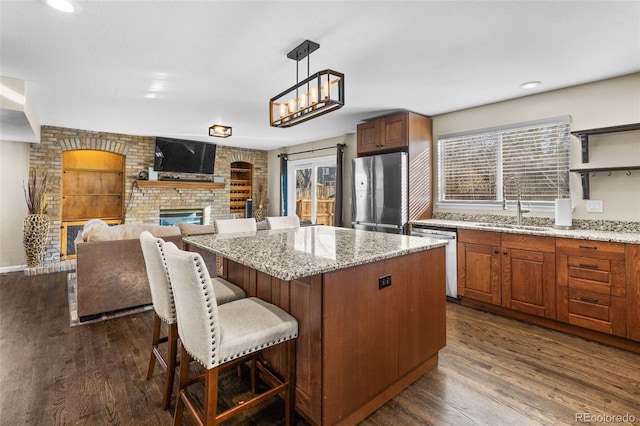 kitchen with a brick fireplace, stainless steel appliances, sink, decorative light fixtures, and dark hardwood / wood-style floors