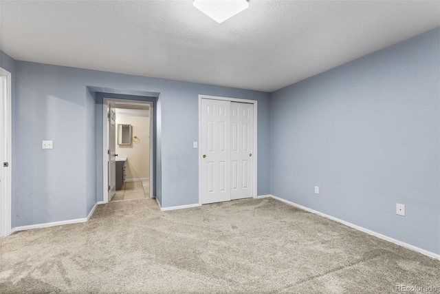 unfurnished bedroom with light carpet, a textured ceiling, connected bathroom, and a closet