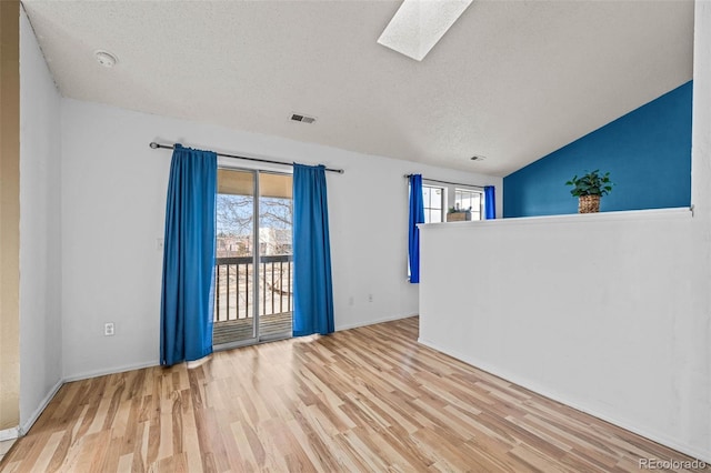 unfurnished room with visible vents, lofted ceiling with skylight, a textured ceiling, and wood finished floors