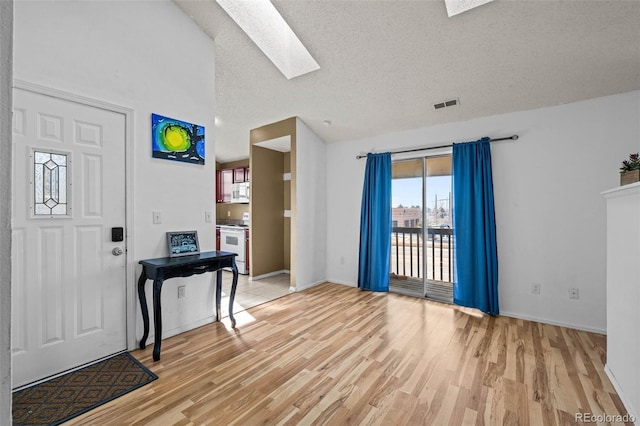 foyer entrance featuring a textured ceiling, light wood finished floors, visible vents, and vaulted ceiling with skylight