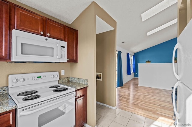 kitchen featuring light tile patterned floors, lofted ceiling with skylight, white appliances, a textured ceiling, and light stone counters