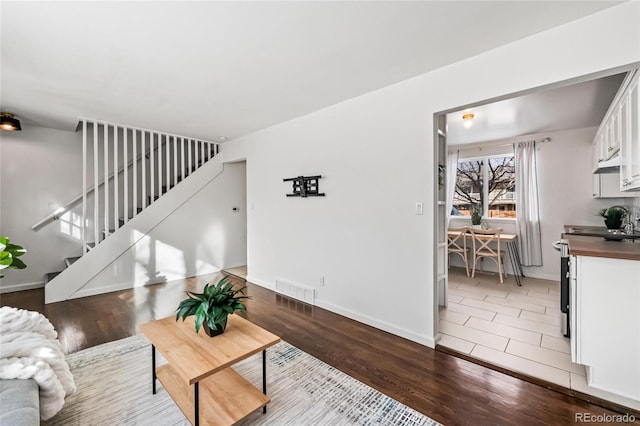 living area featuring baseboards, visible vents, stairway, and wood finished floors