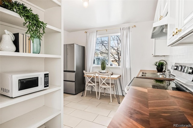 kitchen with white microwave, backsplash, freestanding refrigerator, and white cabinets