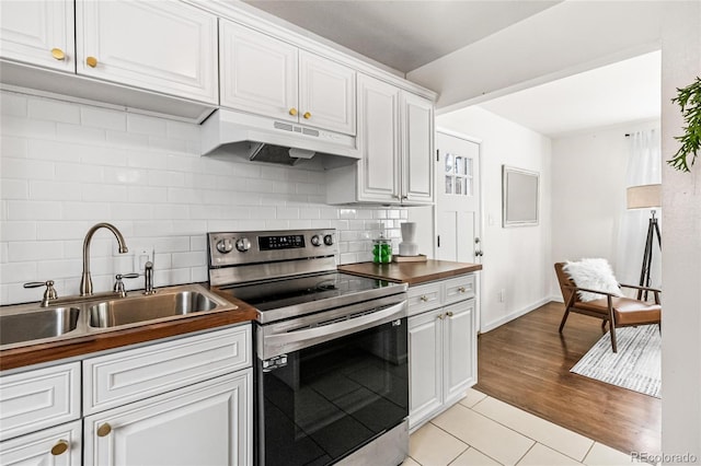 kitchen with tasteful backsplash, white cabinets, electric stove, under cabinet range hood, and a sink