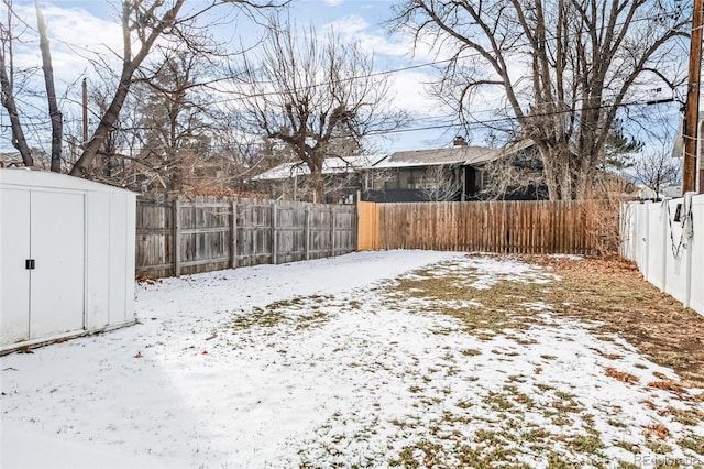 snowy yard with a storage shed, a fenced backyard, and an outbuilding