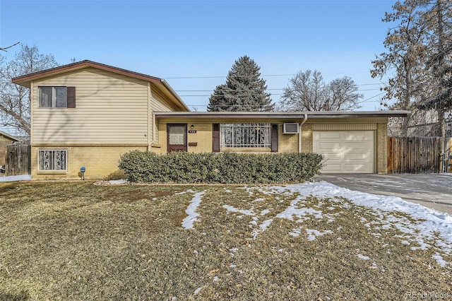 tri-level home with a garage, concrete driveway, brick siding, and fence