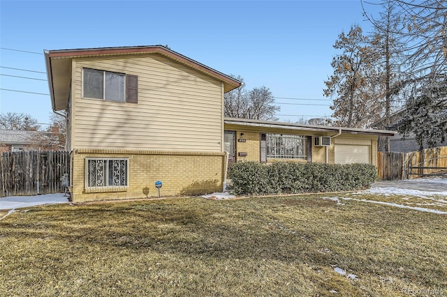 split level home featuring a garage, brick siding, a front lawn, and fence