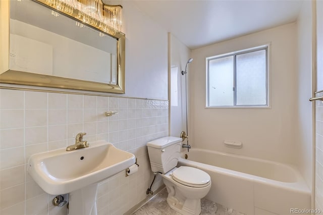 full bathroom featuring a wainscoted wall, tile walls, toilet, a sink, and  shower combination