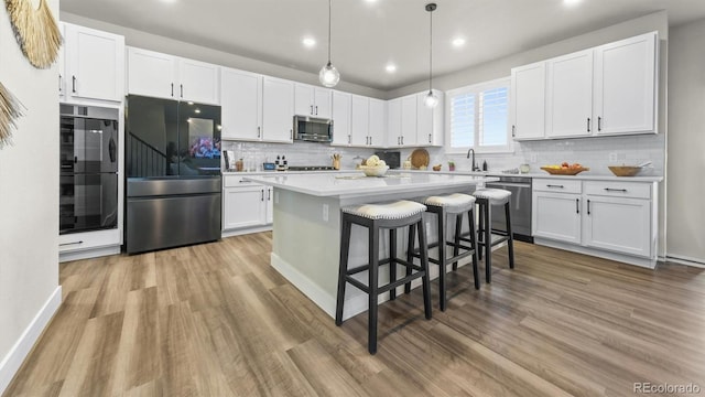 27994 E Indore Dr, Aurora, CO 80016 - kitchen with appliances with stainless steel finishes, light wood-style floors, white cabinets, a kitchen breakfast bar, and recessed lighting