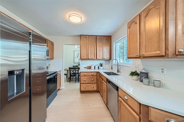 kitchen with tasteful backsplash, appliances with stainless steel finishes, sink, and light hardwood / wood-style floors