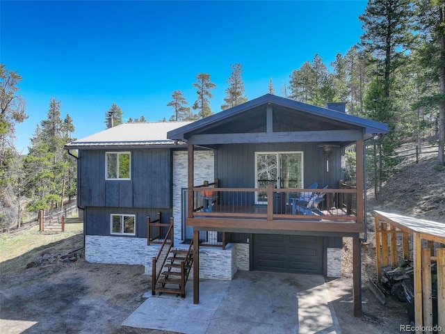 back of property featuring an attached garage, driveway, stone siding, and metal roof