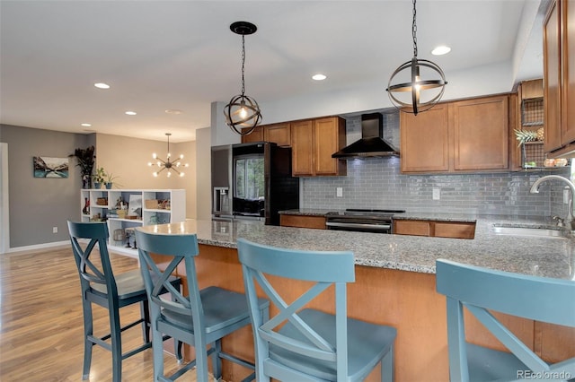 kitchen with wall chimney range hood, brown cabinets, a sink, a chandelier, and backsplash