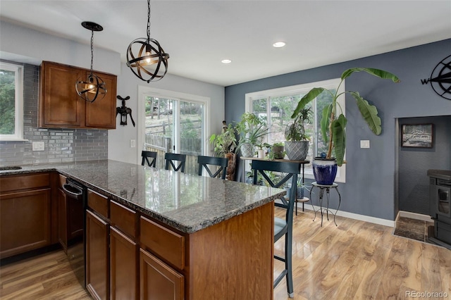 kitchen featuring a kitchen breakfast bar, backsplash, pendant lighting, light wood-type flooring, and dark stone countertops