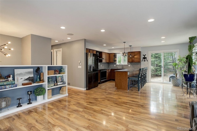 kitchen featuring a kitchen breakfast bar, an inviting chandelier, black appliances, and light wood-style floors