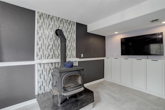 living room with baseboards, visible vents, a textured wall, and a wood stove