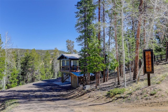 view of front facade with a wooden deck, driveway, a wooded view, and metal roof