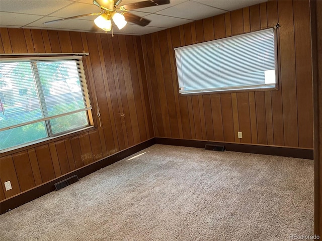 carpeted spare room featuring a drop ceiling, wooden walls, and ceiling fan