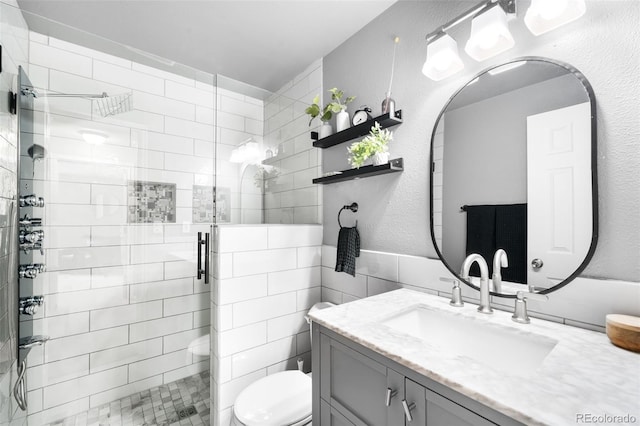 full bathroom featuring vanity, toilet, a textured wall, and a stall shower