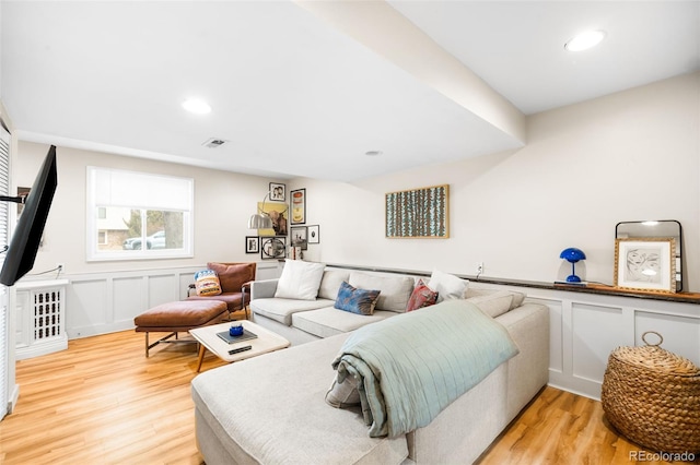 living area featuring light wood finished floors, a decorative wall, recessed lighting, and visible vents