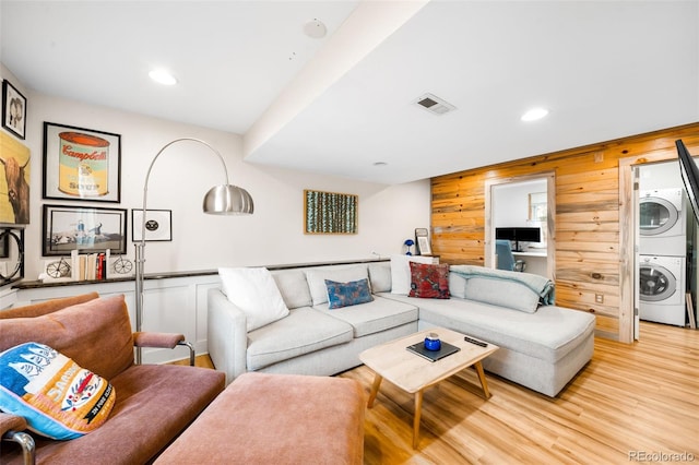 living area with light wood-type flooring, visible vents, stacked washing maching and dryer, recessed lighting, and wood walls