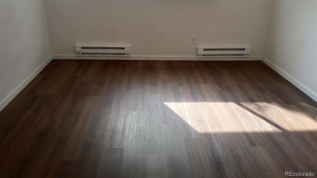 empty room with baseboard heating and dark hardwood / wood-style flooring