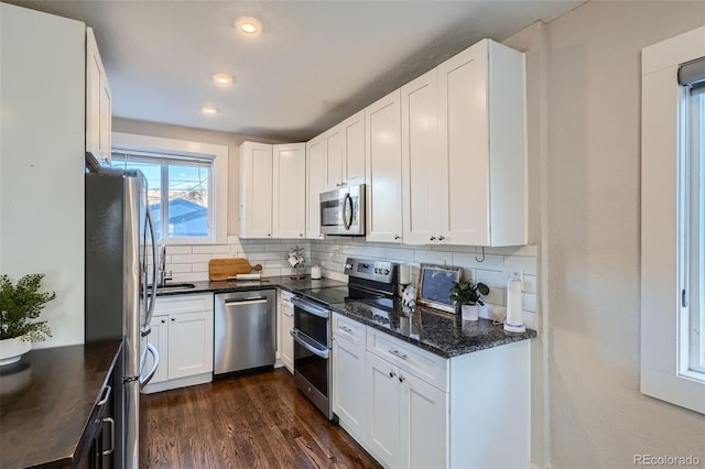 kitchen featuring dark hardwood / wood-style floors, white cabinetry, dark stone countertops, backsplash, and stainless steel appliances