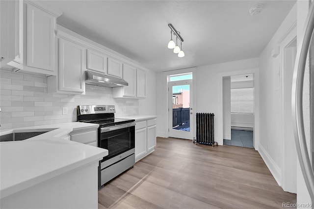 kitchen featuring decorative light fixtures, light wood-type flooring, radiator, stainless steel appliances, and white cabinets