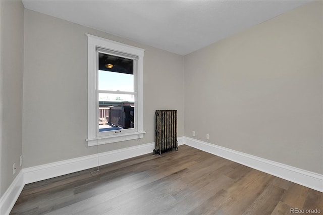 spare room featuring radiator heating unit, baseboards, and wood finished floors